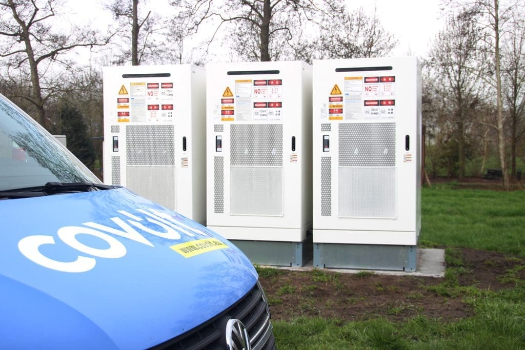 A Covolt service technician next to three battery energy storage systems (BESS) at an outdoor site in Belgium